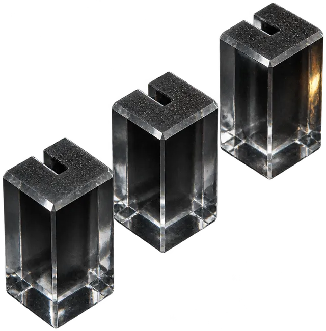 Three clear glass crew pieces, short square pillars with a notch in the top, standing in a diagonal row.